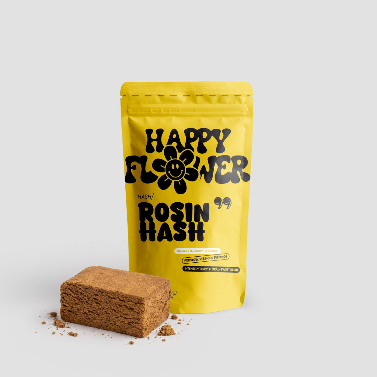 Happy Flower Rosin Hash in gelber Standbeutel-Verpackung mit einem rechteckigen, hellbraunen Hasch-Stück und kleinen Krümeln auf hellem Hintergrund.
